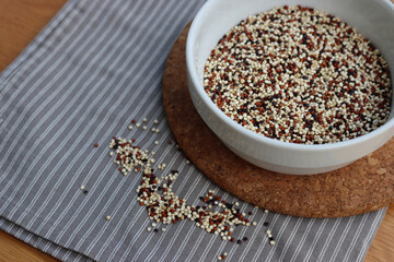Close-up of mix of raw black, red and white quinoa seeds in a ceramic bowl on wooden table