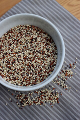 Top view of mix of raw black, red and white quinoa seeds in a ceramic bowl on wooden table