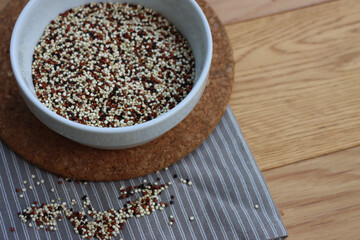 Close-up of mix of raw black, red and white quinoa seeds in a ceramic bowl on wooden table