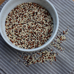 Top view of mix of raw black, red and white quinoa seeds in a ceramic bowl on wooden table