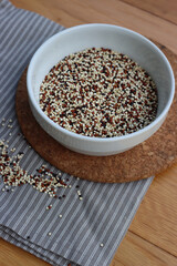 Close-up of mix of raw black, red and white quinoa seeds in a ceramic bowl on wooden table