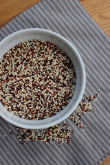 Top view of mix of raw black, red and white quinoa seeds in a ceramic bowl on wooden table