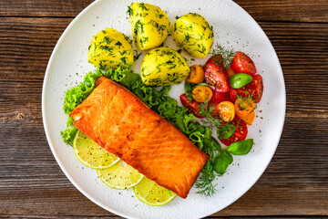 Seared salmon steak with cherry tomato salad and boiled potatoes on wooden table	