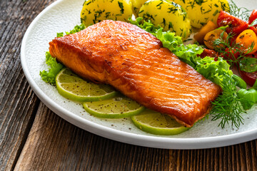 Seared salmon steak with cherry tomato salad and boiled potatoes on wooden table	