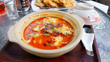 Spicy Asian soup served in a clay pot, filled with fresh red broth, soft tofu, vegetables, and chili oil. Culinary concept, restaurant, or traditional food.