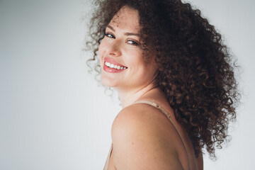 Charming woman with curly hair smiling in natural beauty on a soft white background, celebrating body positivity and self acceptance.