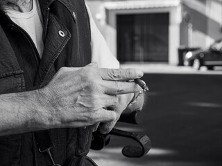 older caucasian man sits on medical walker outdoors, smoking a cigar in public despite visible...