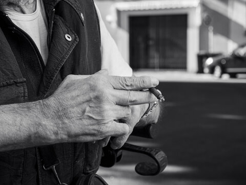 older caucasian man sits on medical walker outdoors, smoking a cigar in public despite visible signs of frailty, illustrating contrast between age-related vulnerability and risky personal habits.