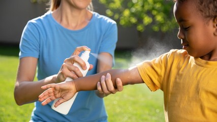 Obraz premium Adult applying mosquito repellent spray to child’s arm in park, insect bite prevention with topical protective solution