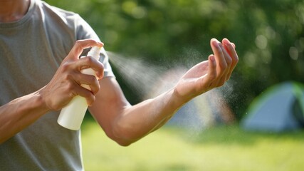 Person applying mosquito repellent spray to arm outdoors, prevention of insect bites during camping or summer activities