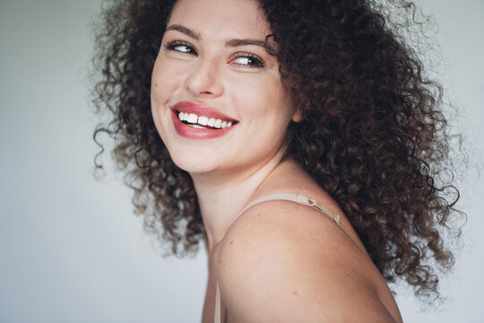 Sensual charming woman with natural beauty smiling warmly in closeup portrait with curly hair and casual lingerie