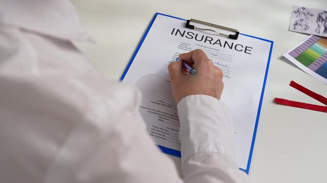 Person Signing an Insurance Document with a Blue Pen