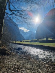 Alpine valley river flowing under bright sun with snow-capped mountains in the background