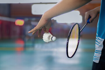 Badminton player holds racket and white cream shuttlecock in front of the net before serving it to...