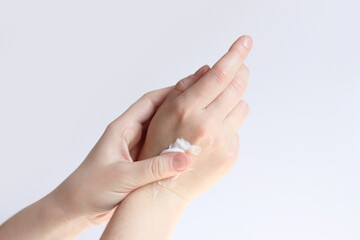 Hand cream. Close-up of young woman's hands with moisturizing cream. Skin care. Woman applying cream on her hands, light background. Healthy skin. Cosmetology. Daily routine