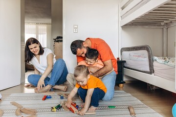 Parents playing and laughing with their two sons in a bright children room. Family bonding, playful...