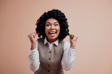 Fototapeta premium Portrait of a cheerful professional woman celebrating a success against beige background, expressing accomplishment and joy