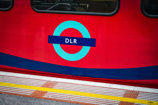 West India Quay DLR Train Logo Sign, Docklands Light Railway Vehicle At Station Roundel Signage, North Dock, Canary Wharf, East London Borough Tower Hamlets, London Docklands, England, UK, June 2025