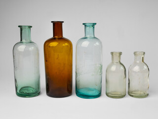 Vintage apothecary glass jars in a row close-up on white background. Antique colored glassware 