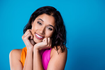 Fototapeta premium Portrait of a young woman with a charming smile and hands on cheeks against a vibrant blue background