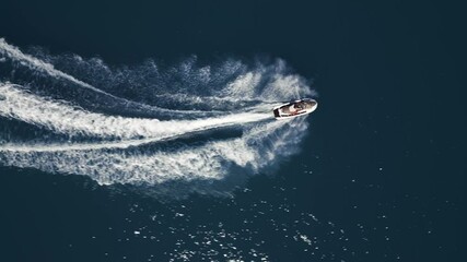 Aerial view of a jet ski speeding across dark blue water, leaving a dynamic white trail. Captured by drone from above, showcasing motion, power, and summer fun on the sea