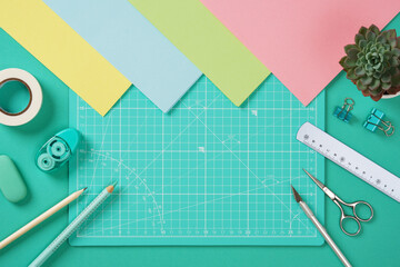 Top view of a desk for paper crafts. Pencil, glue, eraser, knife, scissors, and colored paper.