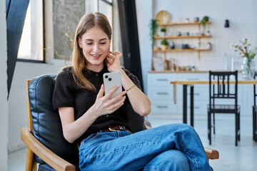 Young woman sitting at home on chair using smartphone
