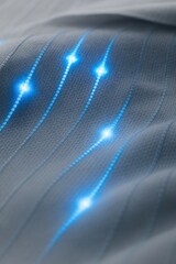 A macro photo of futuristic smart textile with glowing blue light fibers embedded in soft grey fabric. The illuminated lines follow a subtle wave pattern and emit soft pulses of light at intervals