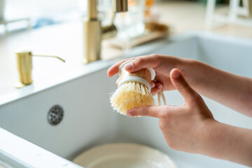 Closeup of children's hands washing a plate near the sink in the kitchen. Eco dishwashing brush.