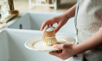 Closeup of children's hands washing a plate near the sink in the kitchen. Eco dishwashing brush.