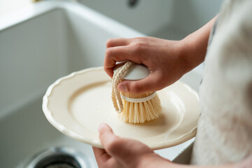 Closeup of children's hands washing a plate near the sink in the kitchen. Eco dishwashing brush.