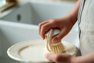 Closeup of children's hands washing a plate near the sink in the kitchen. Eco dishwashing brush.