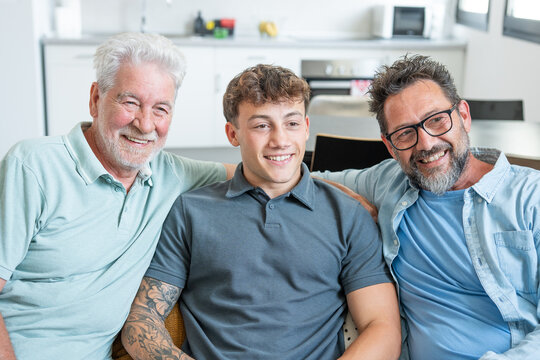 Happy multigenerational family of males stay together sitting on sofa smiling. Grandfather, mature son and young grandson share positive moments in total relax