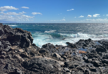 Rocky beach on a black volcanic landscape in Tenerife, Canary  islands in a sunny windy day, the ocean waves crash on the coast, horizon over water