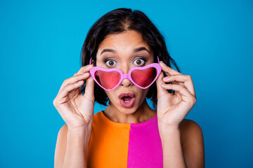 Young woman posing with vibrant pink heart-shaped sunglasses, expressing playful surprise