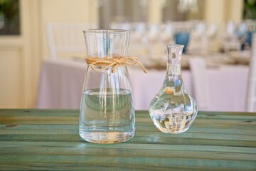Glass vases filled with water and tied with string sit on a wooden table, ready for floral arrangements at a wedding reception