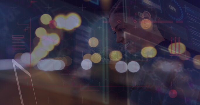 Image of illuminated lens flare and graphical interface over businesswoman using laptop