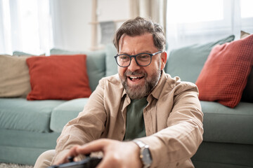 Fototapeta premium Excited mature man playing videogames at home in living room