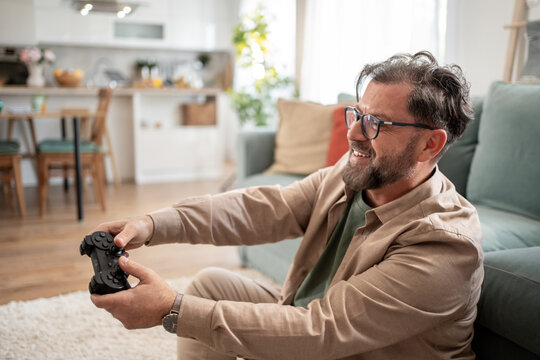 Happy bearded man playing videogames at home sitting on the floor