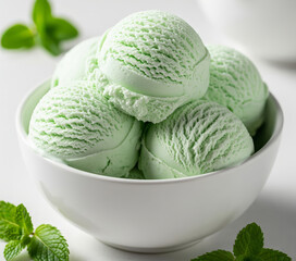 Close-up of a white bowl filled with three scoops of mint ice cream, garnished with a fresh mint leaves