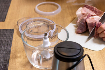 Woman cuts the meat, prepares it to grind it in electrical chopper. Food