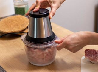 Woman mince the meat in the electrical chopper on the kitchen counter top. Cooking