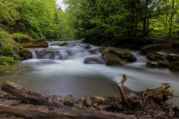 Waterfall in the mountains, river rapids, fast flow, Scenic view of pristine Carpathian nature with crystal clear water cascading over mossy rocks. Photo wallpaper, beauty of nature and the Earth.