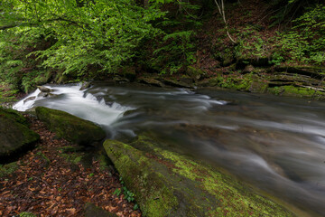 Waterfall in the mountains, river rapids, fast flow, Scenic view of pristine Carpathian nature with crystal clear water cascading over mossy rocks. Photo wallpaper, beauty of nature and the Earth.