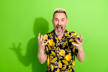 Middle aged man with funky dyed hair and stylish summer shirt expressing excitement on green...