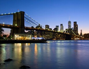 Fototapeta premium Night view of Brooklyn Bridge and Manhattan skyline reflecting on calm water. Serene dusk scene.