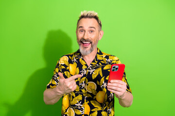 Middle aged man with vibrant style holding red smartphone on green background, exuding summer vibes...