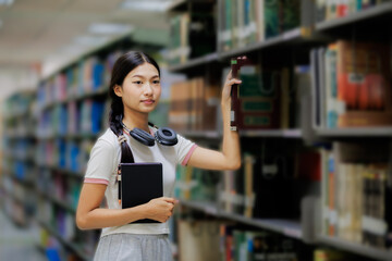 A female student is browsing books on a shelf in the library, focused on finding the right material for her studies.