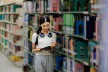 A female student is browsing books on a shelf in the library, focused on finding the right material for her studies.