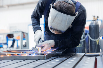 Male industrial worker welding metal in factory setting